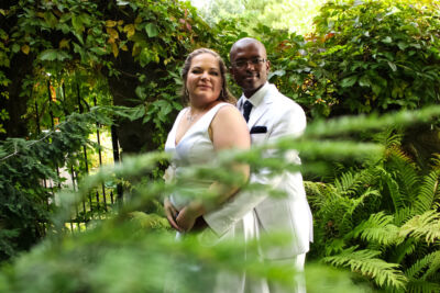 Jeunes mariés posant avec l'homme enlaçant sa femme dans un décor verdoyant